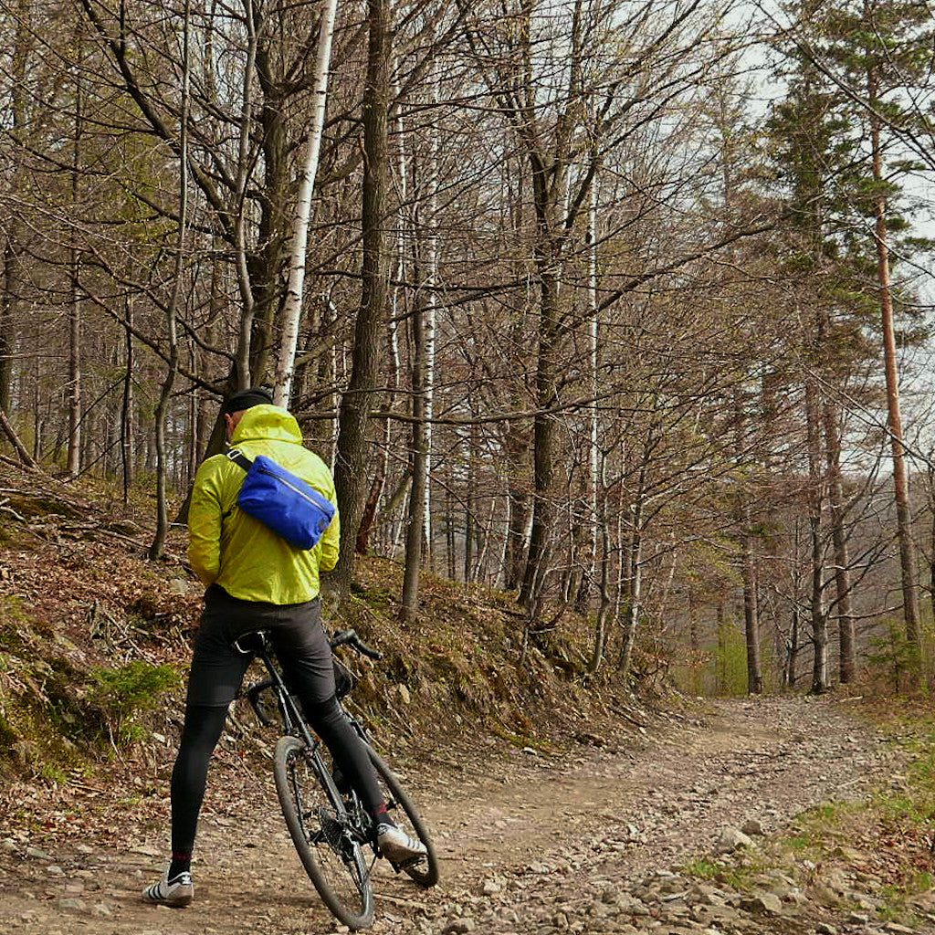 Cyclist riding through the forest with a big cobalt sling bag