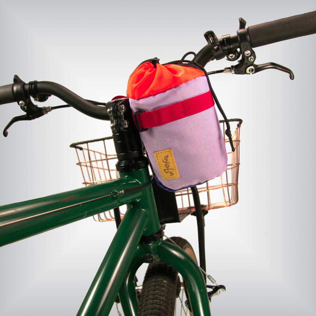 A bright lilac and purple feed bag attached to a MTB bicycle's handlebars.