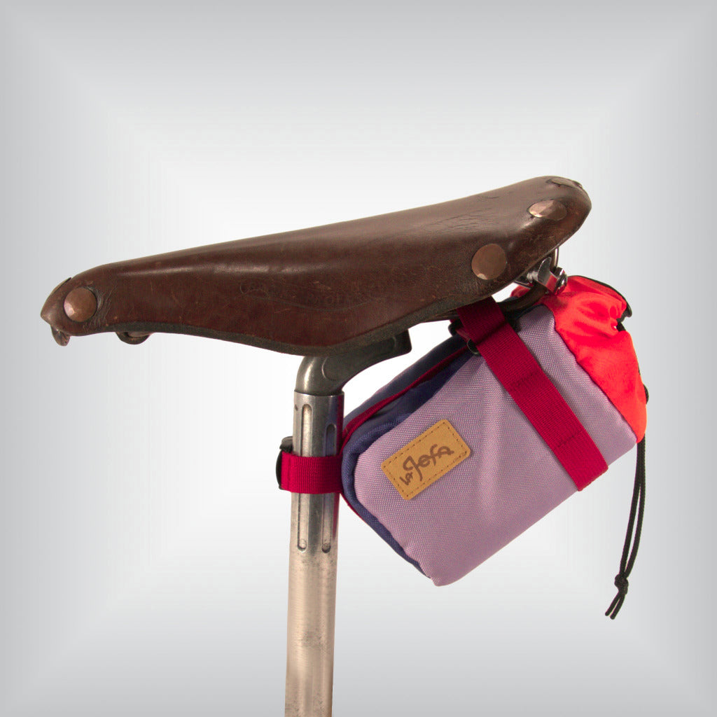 A colourful feed bag attached to vintage leather bicycle saddle.